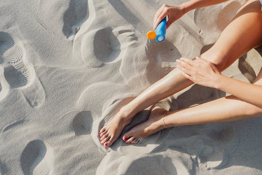  A woman at the beach applying lotion to her legs