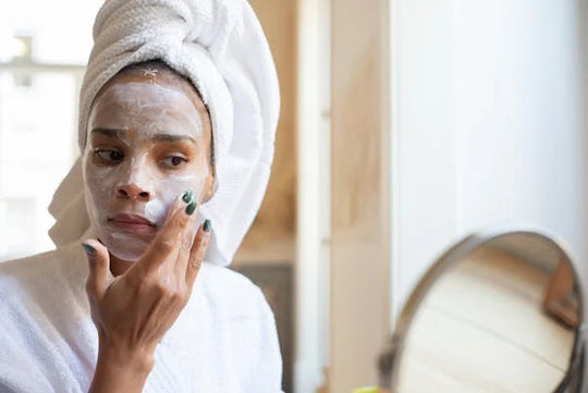 women adjusting her skincare routine when moving, sitting in front of a mirror with a towel wrapped around her hair